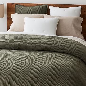 a bed with green and white comforter next to two lamps on either side of the headboard