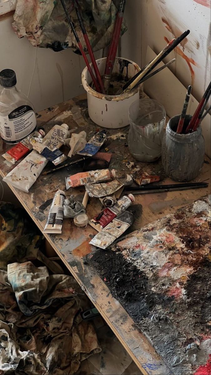 an artist's desk with lots of paint and brushes