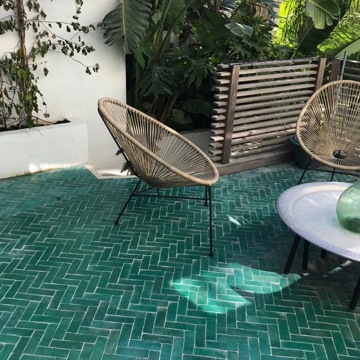 two wicker chairs sitting on top of a green tiled patio