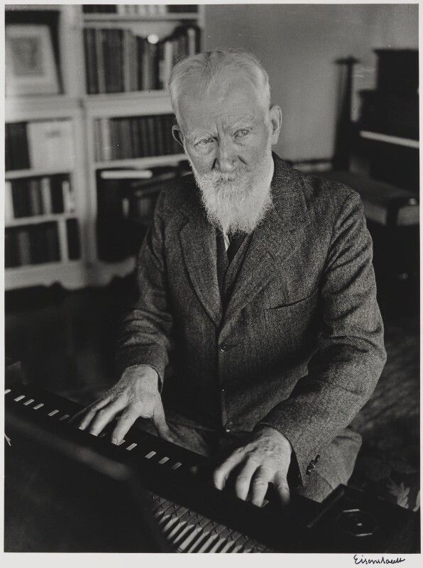 an old man sitting at a piano in front of a book shelf with books on it