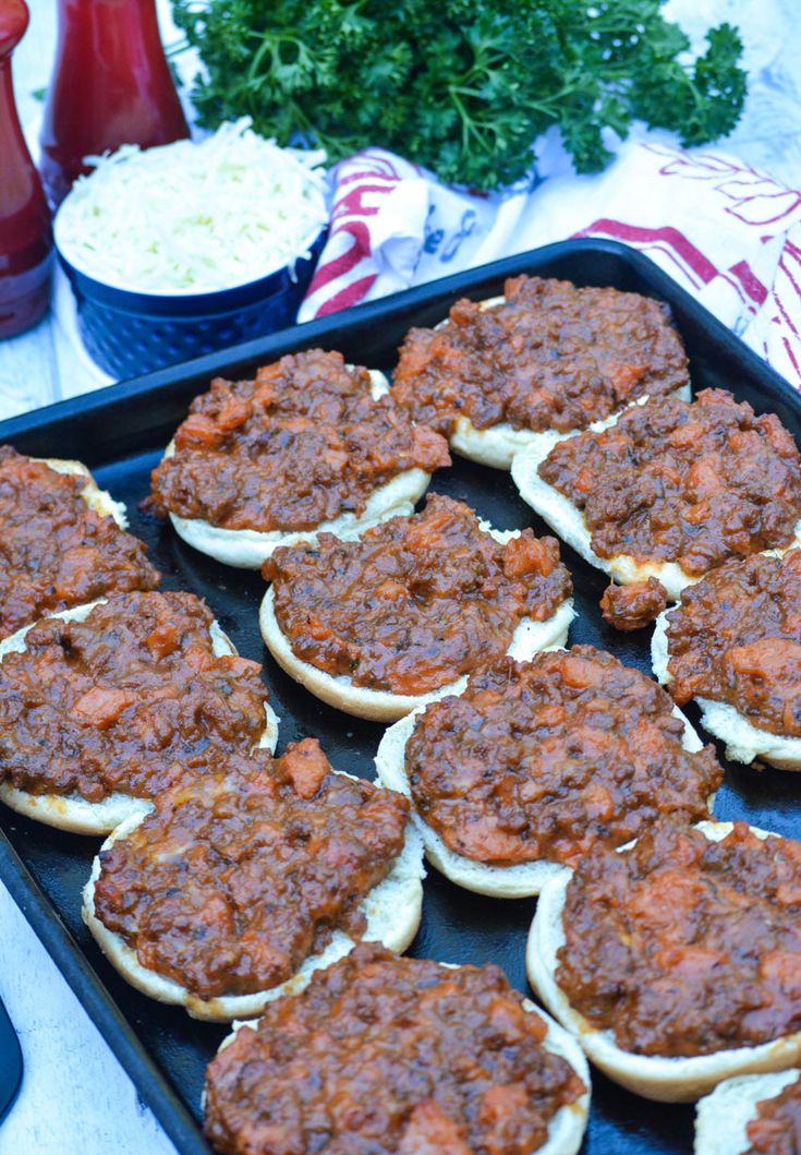 a tray filled with mini sloppy joes covered in cheese and chili next to other food