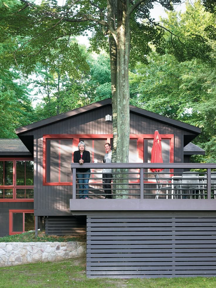 two people standing on a deck in front of a house with red doors and windows