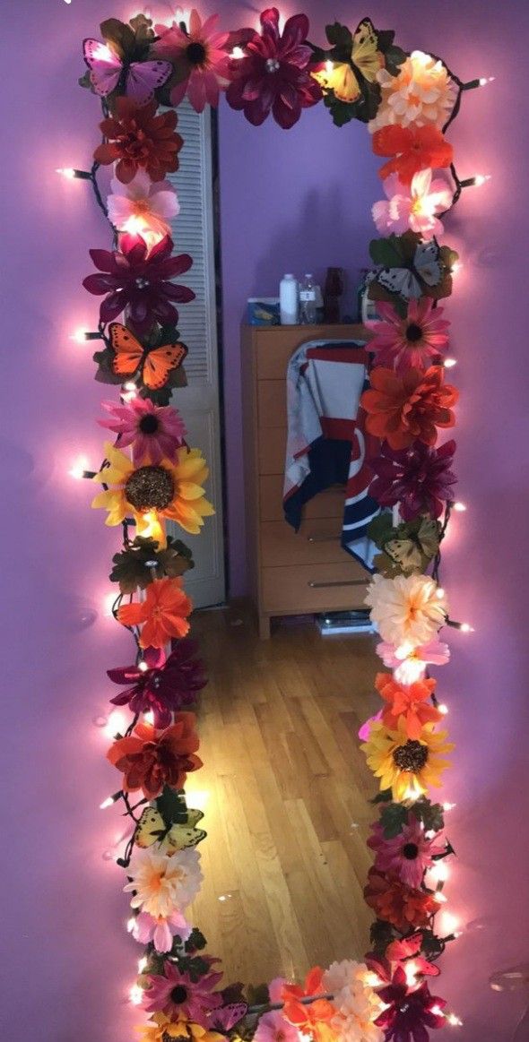 a mirror that has flowers on it and lights in the frame around it, along with other decorations