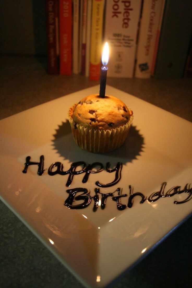 a cupcake with a lit candle sitting on top of a white plate that says happy birthday