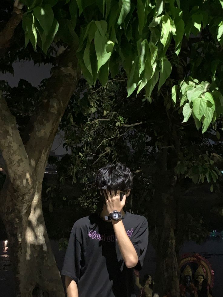 a man standing under a tree talking on a cell phone while holding his hand to his face