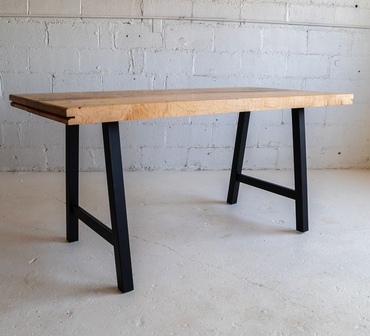 a wooden table sitting in front of a white brick wall with black legs on it