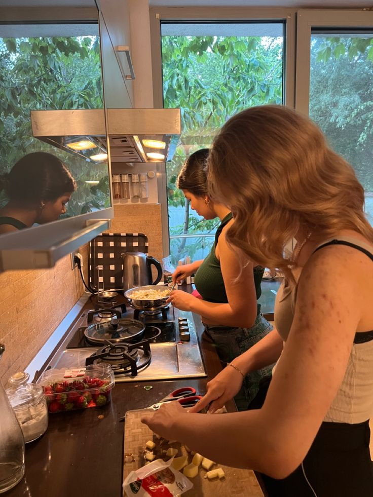 two women preparing food in a kitchen with windows looking out on the trees and water