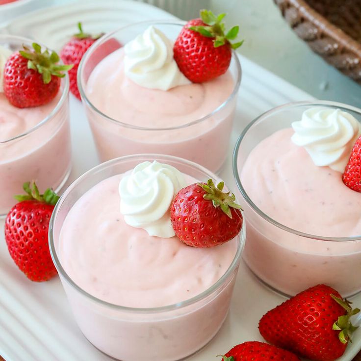 four desserts with strawberries and whipped cream in small cups on a tray, ready to be eaten