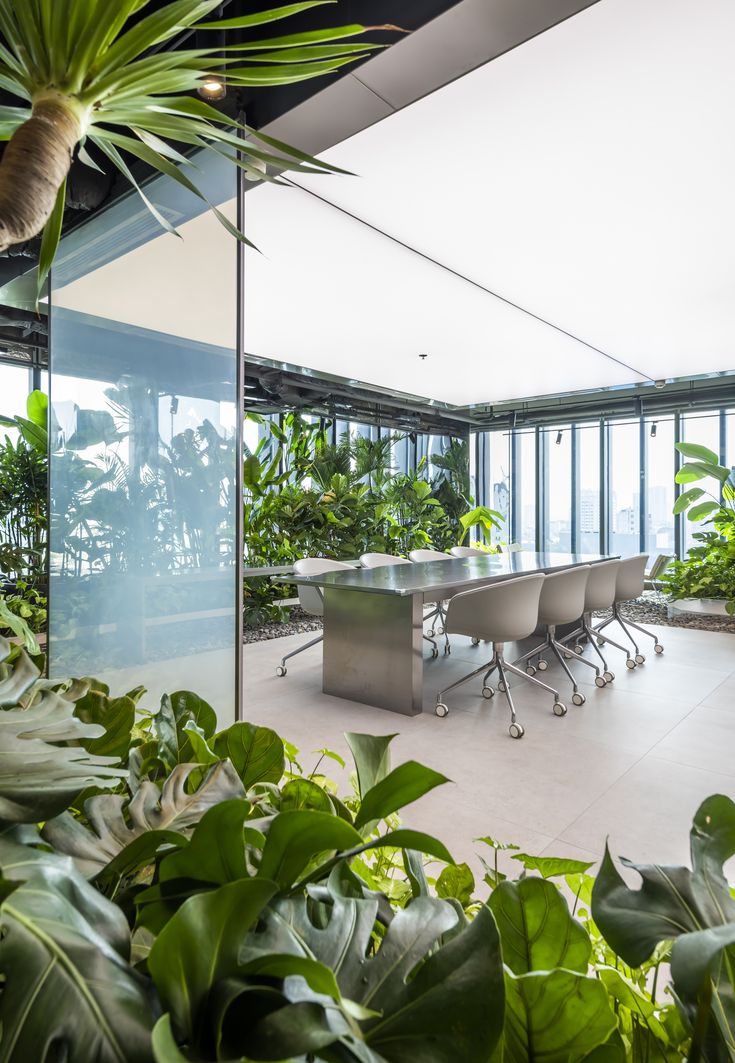 an office with lots of plants in the middle and glass walls on both sides, along with large windows