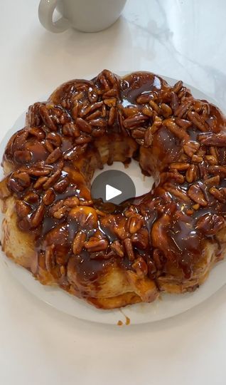 a bundt cake covered in pecans on top of a white plate next to a cup