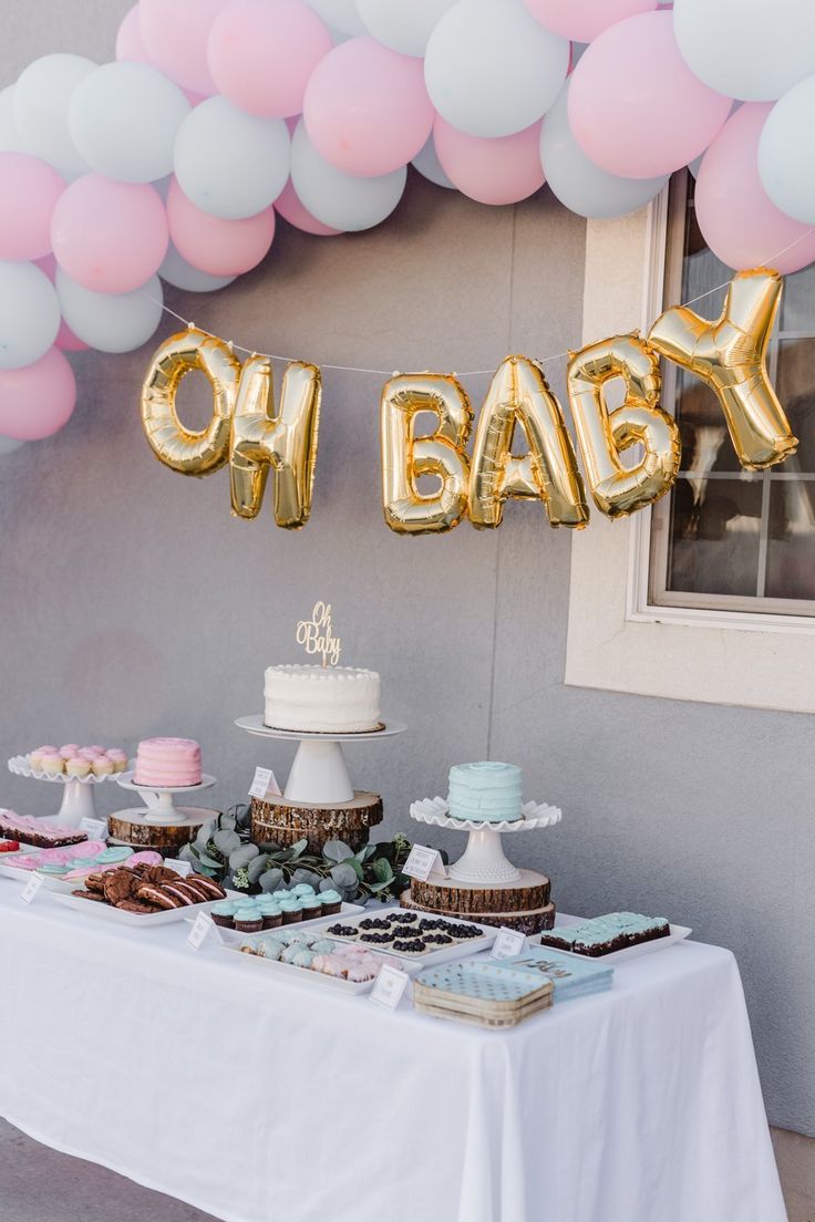 a table topped with cake and balloons that say oh baby in gold letters on top of it