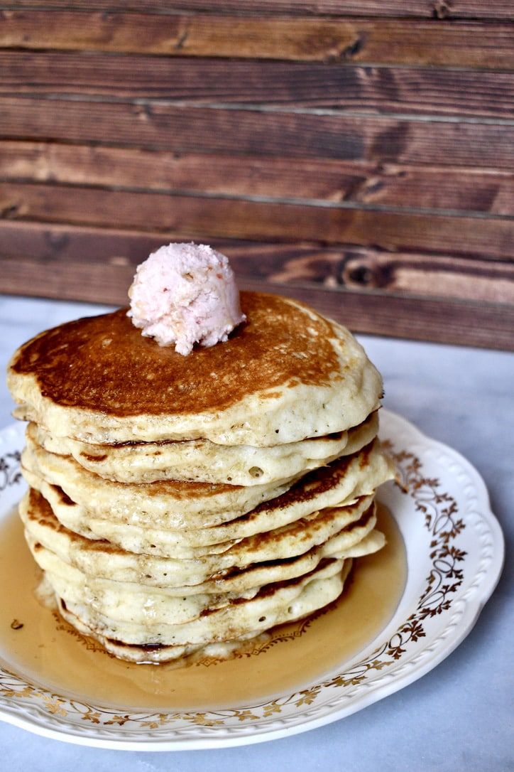 a stack of pancakes topped with butter and syrup on a white plate next to a wooden wall