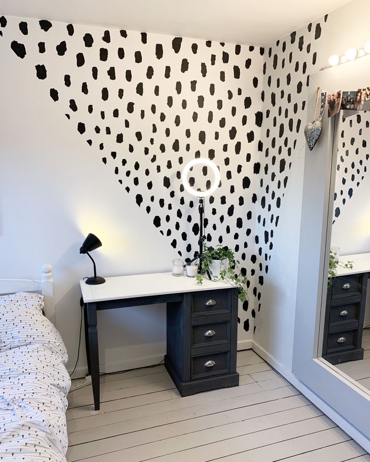 a black and white polka dot wallpaper in a bedroom with a desk, mirror and bed