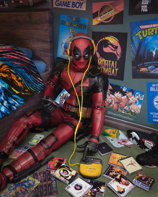 a deadpool doll sitting on the floor surrounded by gameboy memorabilia and video games