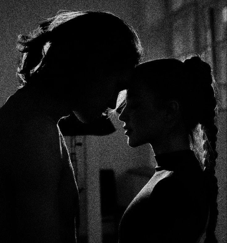 black and white photograph of two people in the dark, one kissing the other's forehead