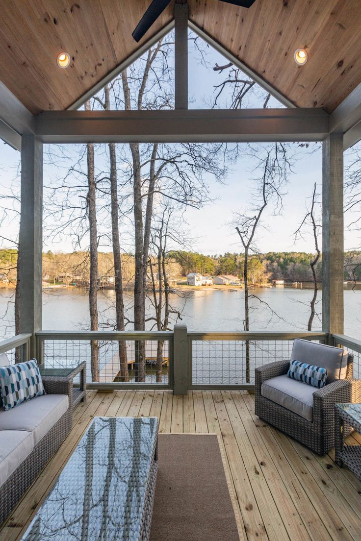 a covered porch with couches and tables on the deck next to trees, overlooking a body of water