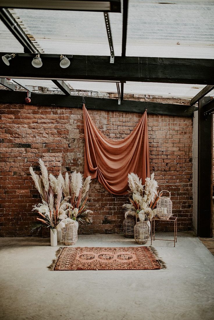 two chairs and some plants in front of a brick wall with drapes on it