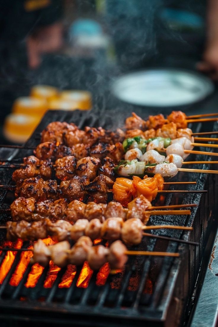 several skewers of food being cooked on a grill with tongs and plates