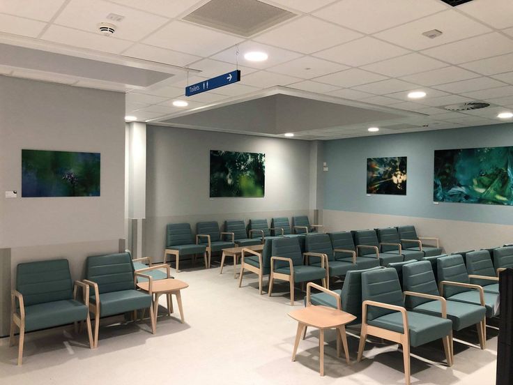 an empty waiting room with blue chairs and pictures on the wall