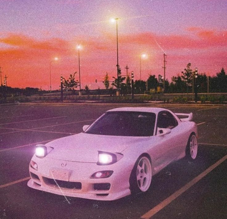 a white sports car parked in a parking lot at night with the sun setting behind it