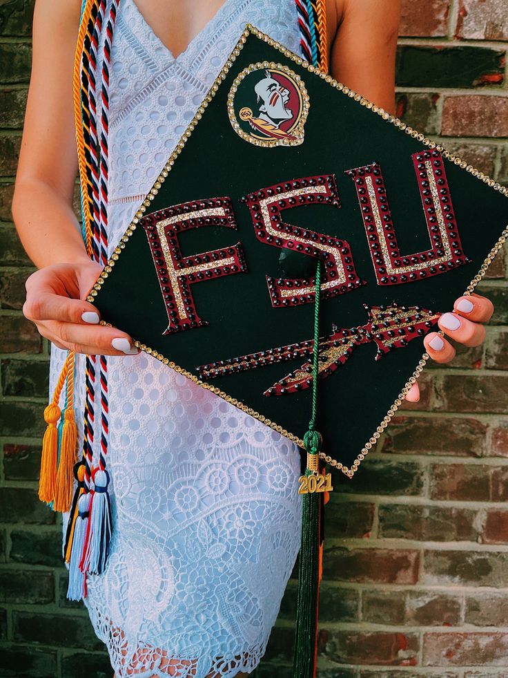 a woman holding a black graduation cap with the word fsu on it and tassels