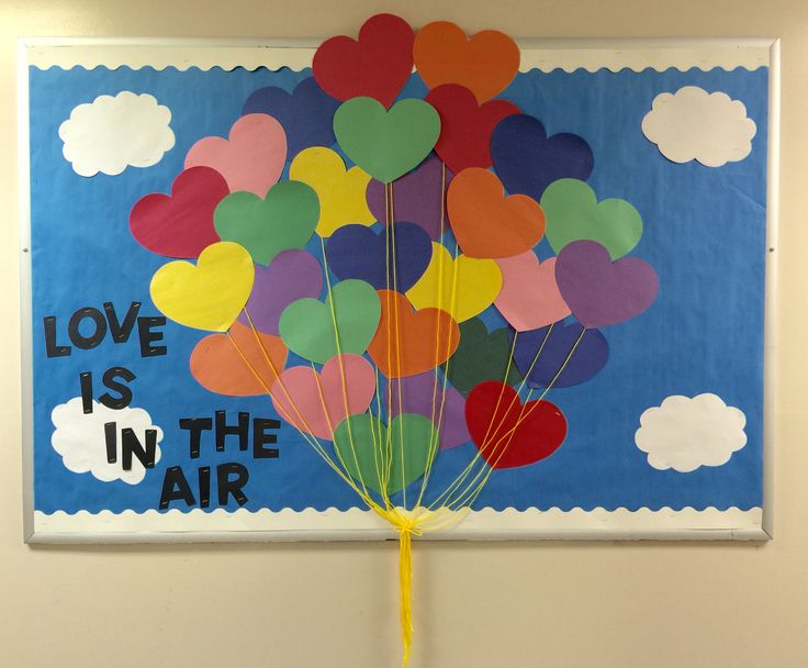 a bunch of heart shaped balloons in front of a bulletin board that says love is in the air