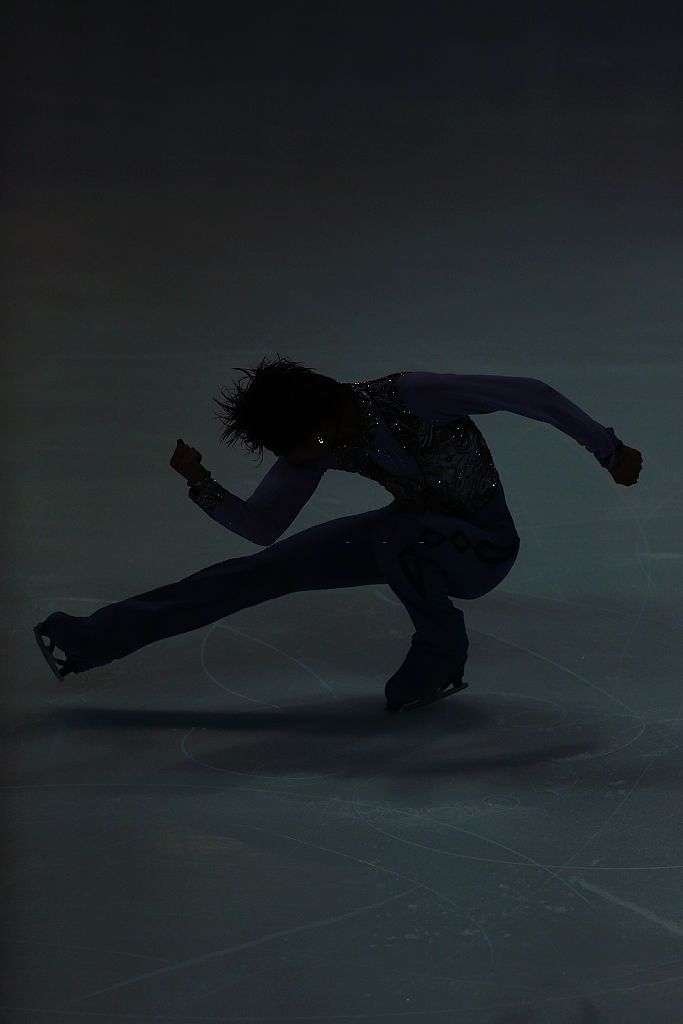 a person skating on an ice rink in the dark with their arms out and legs bent