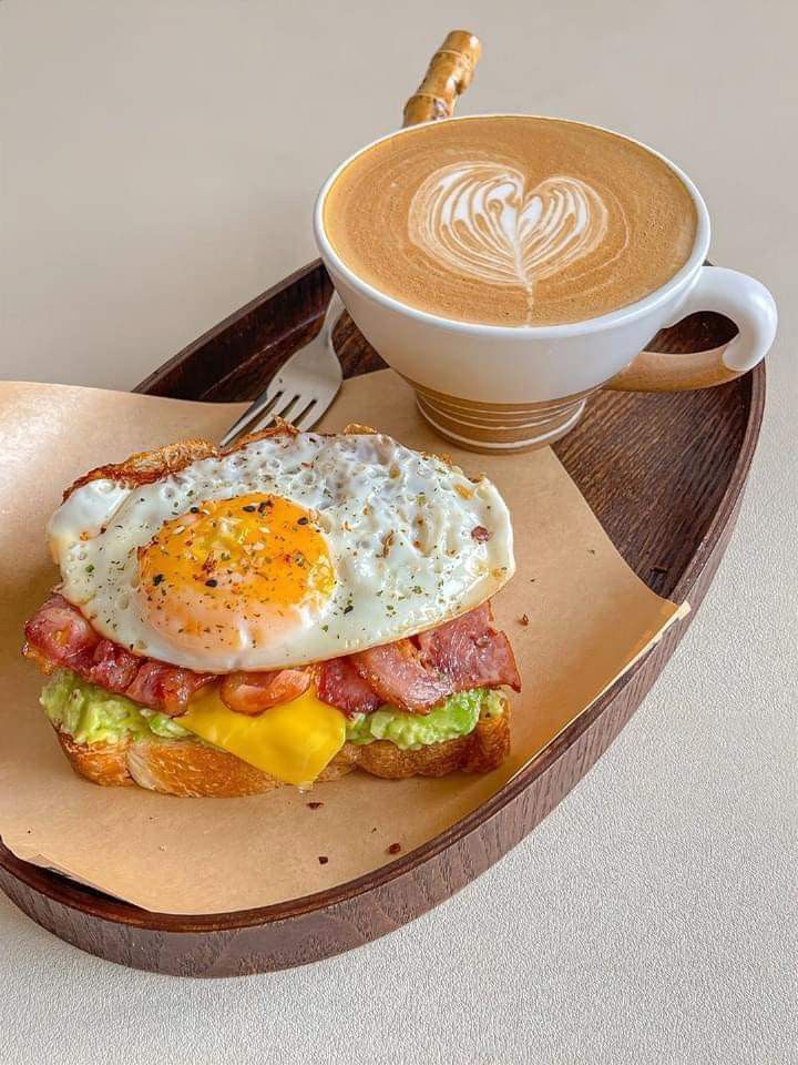 a breakfast sandwich with an egg and bacon on toast next to a cup of cappuccino