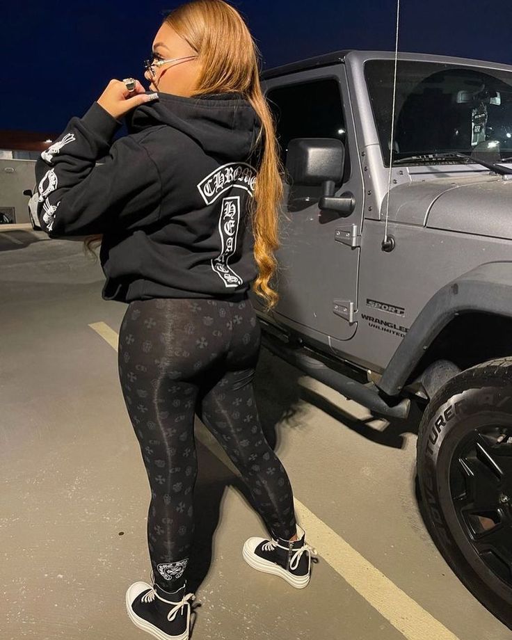 a woman standing next to a gray jeep in a parking lot at night with her phone up to her ear