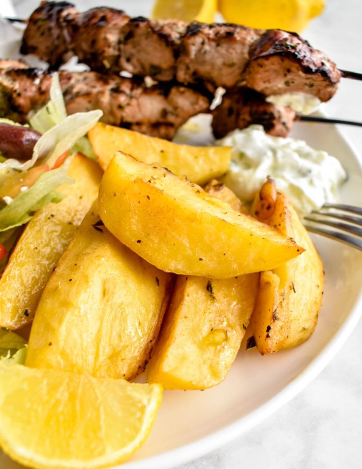 a white plate topped with meat and potatoes next to a lemon wedged potato salad