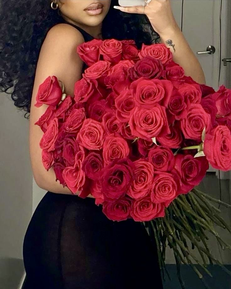 a woman holding a bouquet of red roses in front of her face while taking a selfie