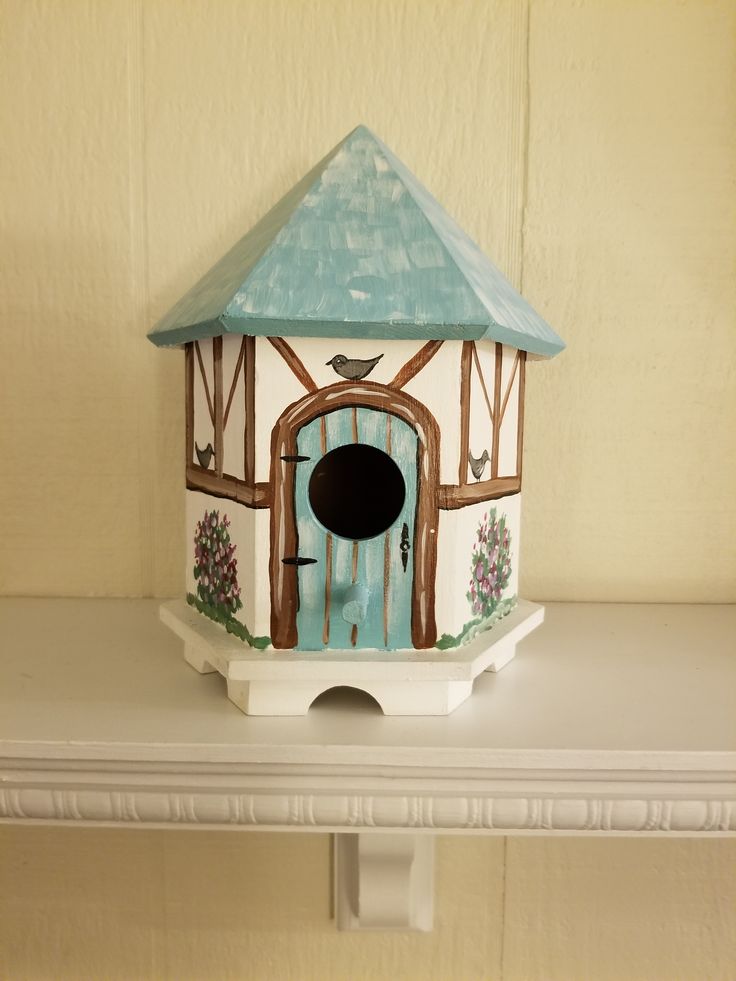 a bird house with a blue roof on top of a white shelf next to a wall