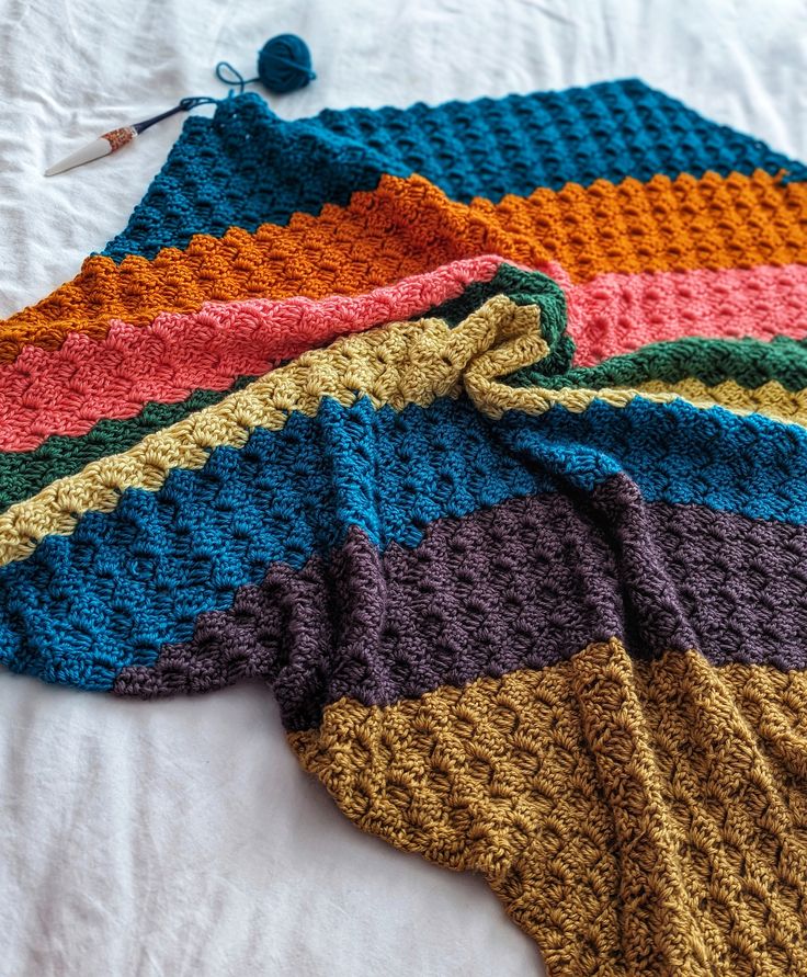 there is a crocheted blanket laying on the bed next to another knitted blanket