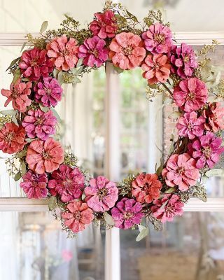 a wreath with pink flowers hanging from the side of a window in front of a door