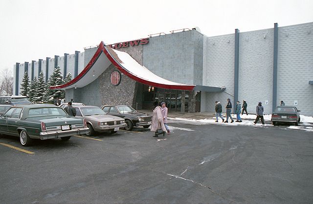 several cars parked in front of a building with people walking around the parking lot near it