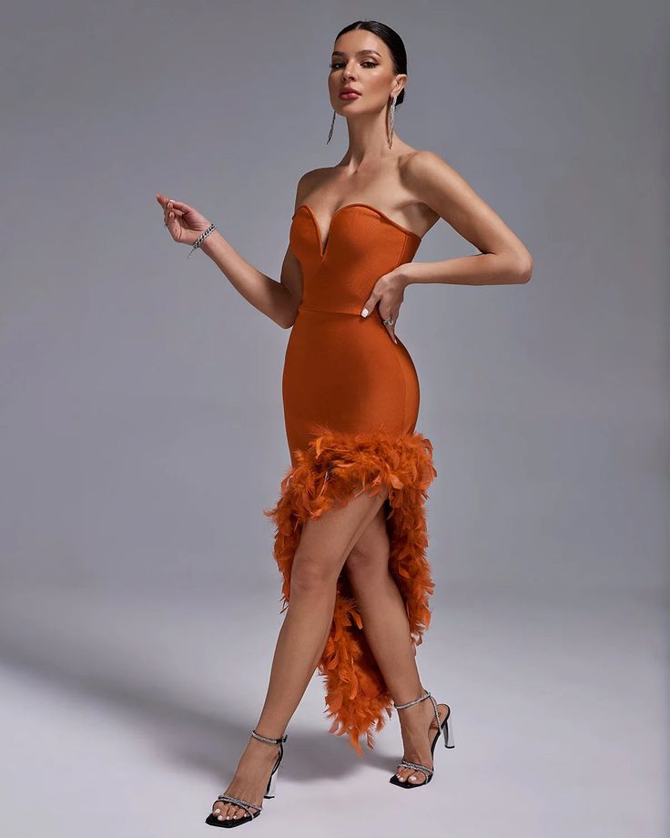 a woman in an orange dress with feathers on the skirt and heels is posing for a photo