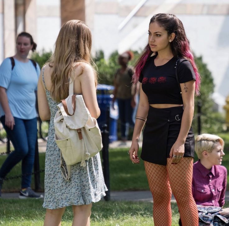 two young women standing next to each other in front of a group of people on the grass