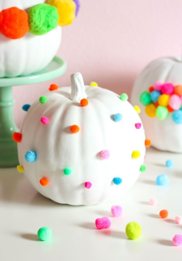 two white pumpkins decorated with colorful pom - poms on a cake stand