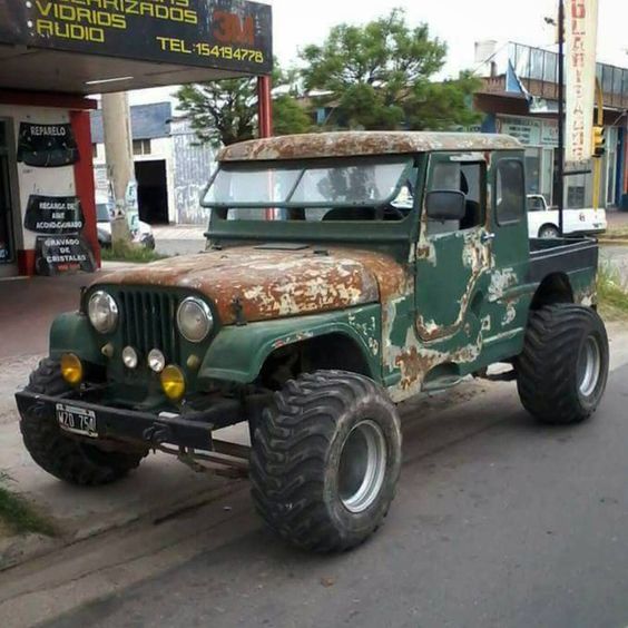 an old green truck is parked on the side of the road in front of a gas station