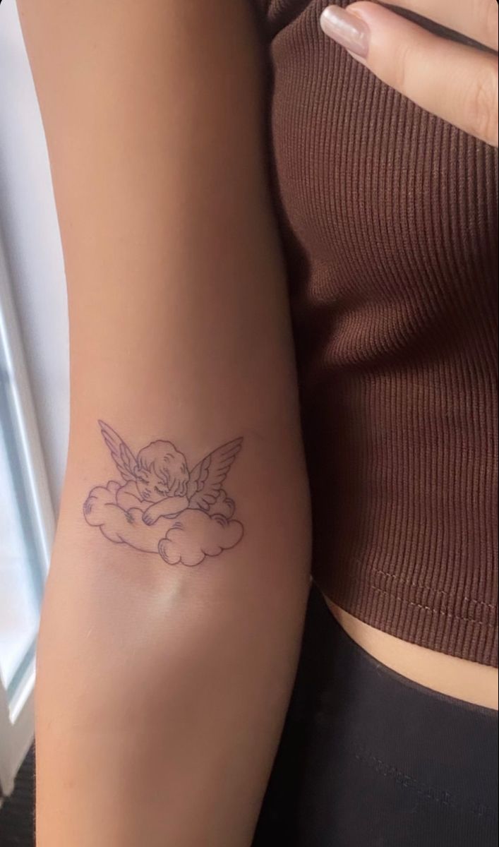 a woman's arm with a tattoo on it that has an angel sitting on the cloud