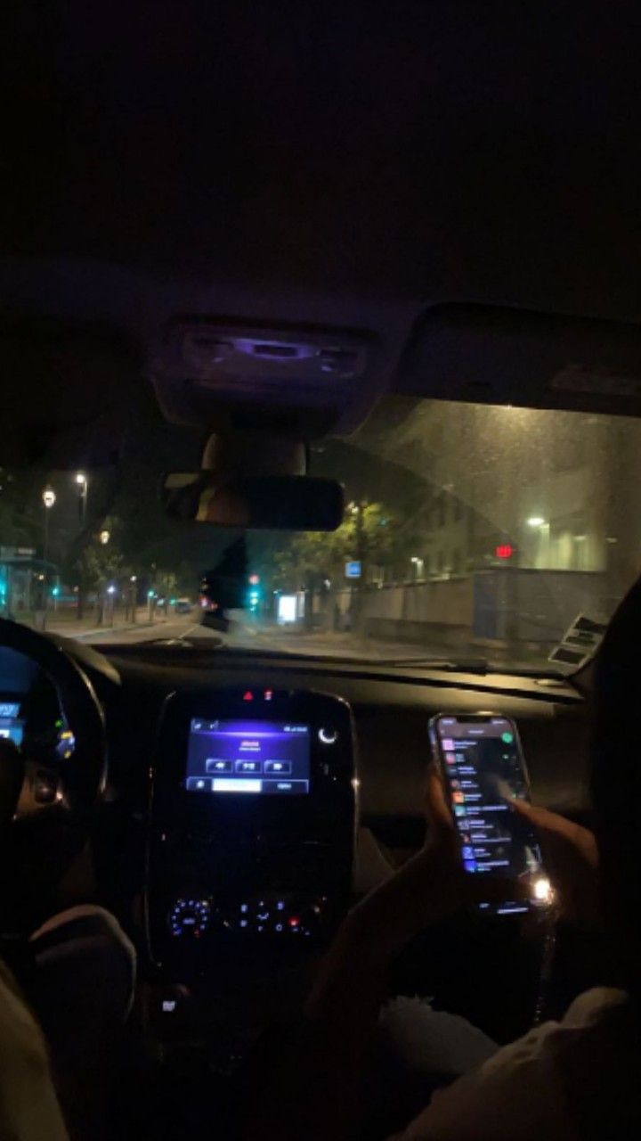 two people using their cell phones while driving in the car at night with lights on