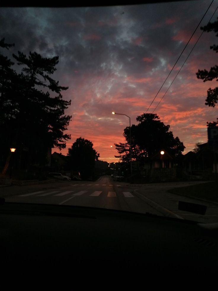 the sun is setting behind some trees and power lines as seen from inside a car