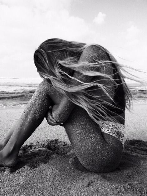 a woman sitting on the beach with her hair blowing in the wind and looking at the ocean