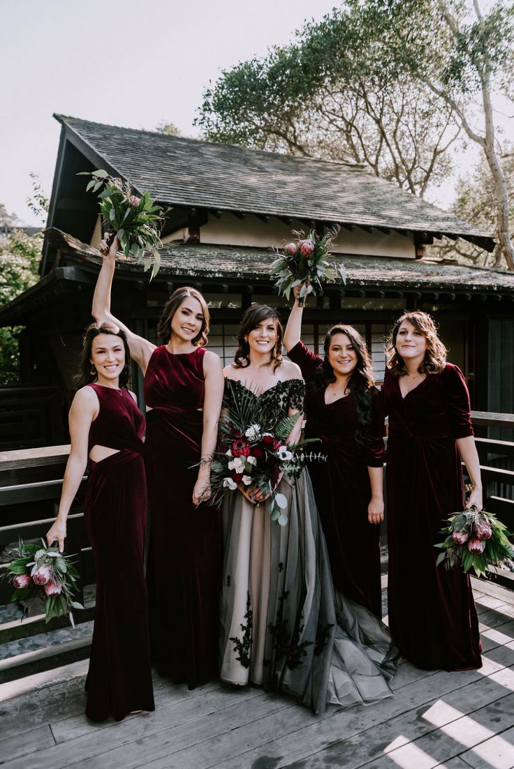 a group of women standing next to each other on a wooden deck holding bouquets