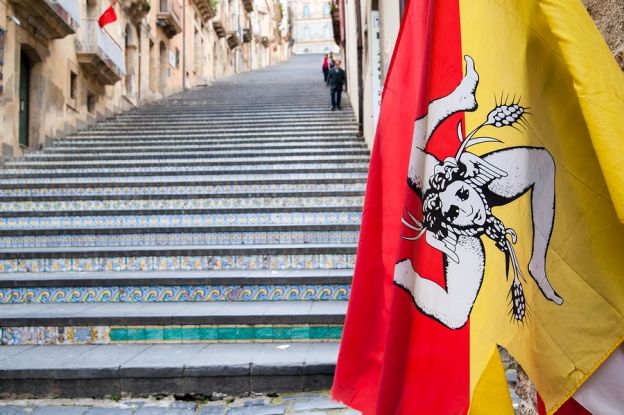 two flags are hanging on the side of some steps in an old european city with stairs leading up to them