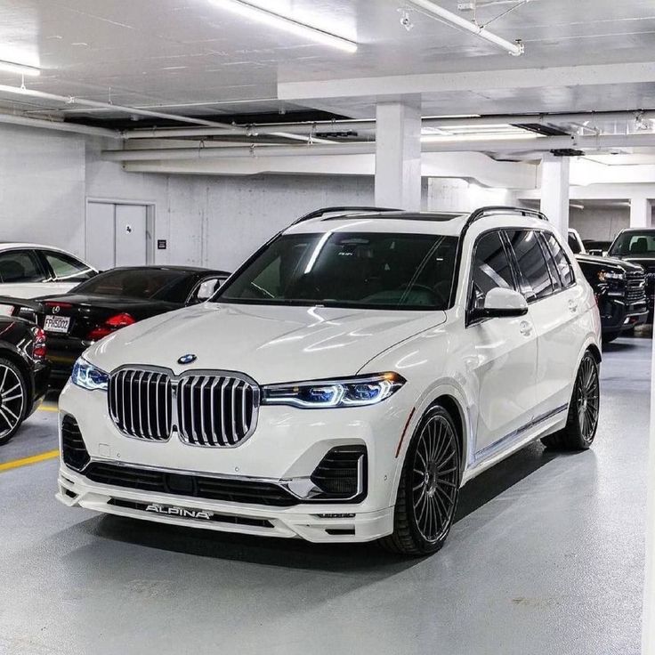 a white bmw suv parked in a parking garage next to other cars on the ground