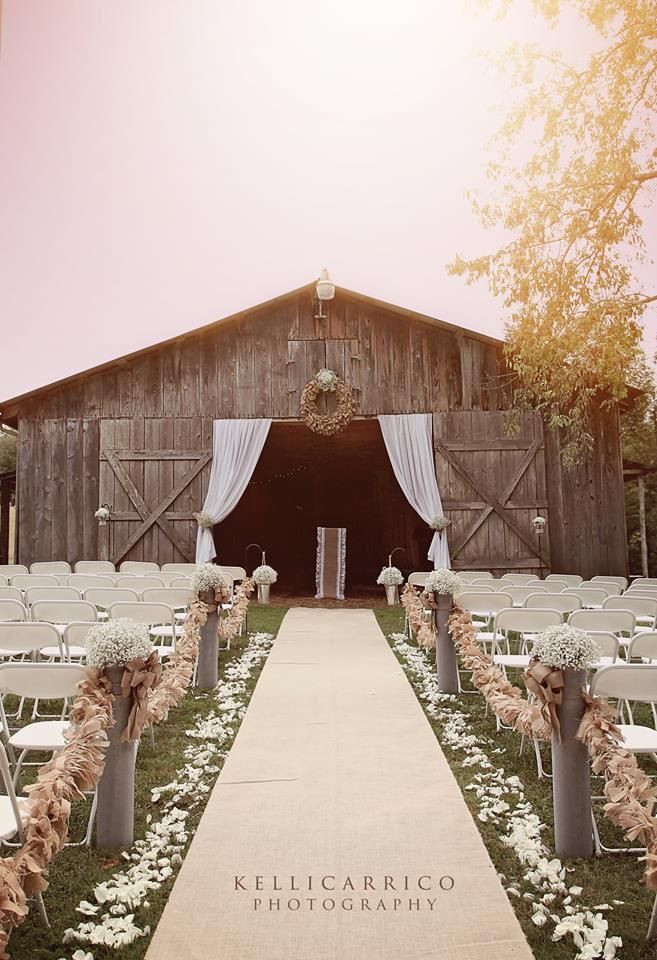 an outdoor ceremony setup with chairs and flowers in front of a wooden barn at sunset