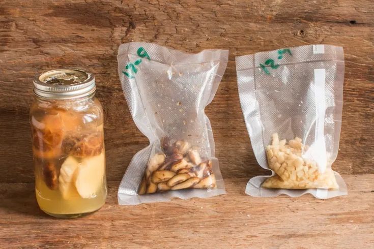 two bags of food sitting next to each other on a wooden table with a mason jar filled with liquid