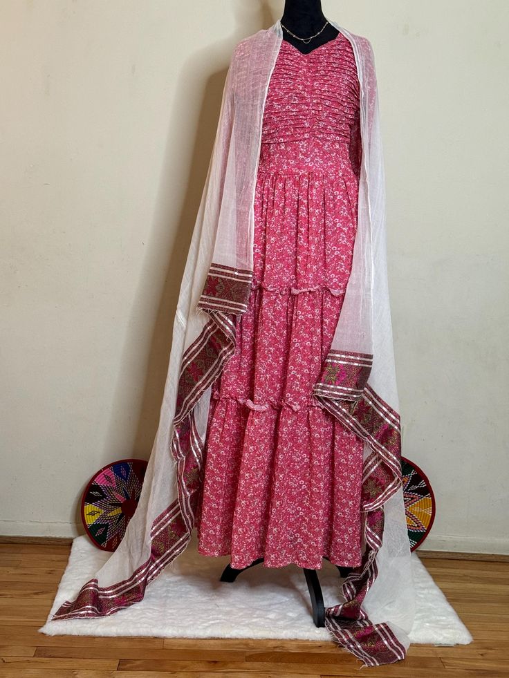 Ethiopian and Eritrean traditional dress (shifon)pink traditional outfit with white and pink details. The ensemble includes a layered dress with a patterned border and a sheer white shawl draped over the shoulders. beautiful shifon Pink Traditional Outfit, Habesha Kemis, White Shawl, Traditional Outfit, Pink Details, Layered Dress, 70 Dress, Traditional Dress, Traditional Dresses