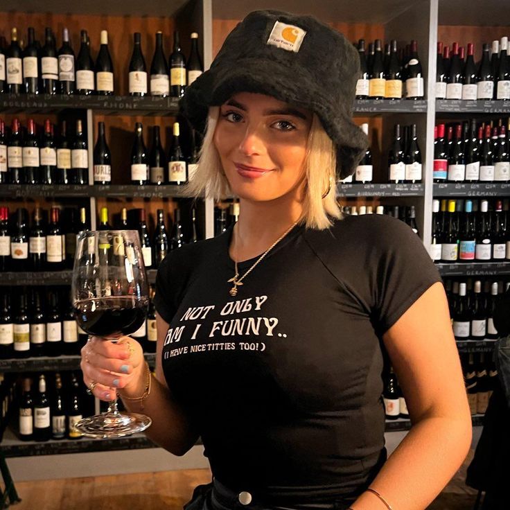 a woman is holding a glass of wine in front of shelves full of bottles and glasses